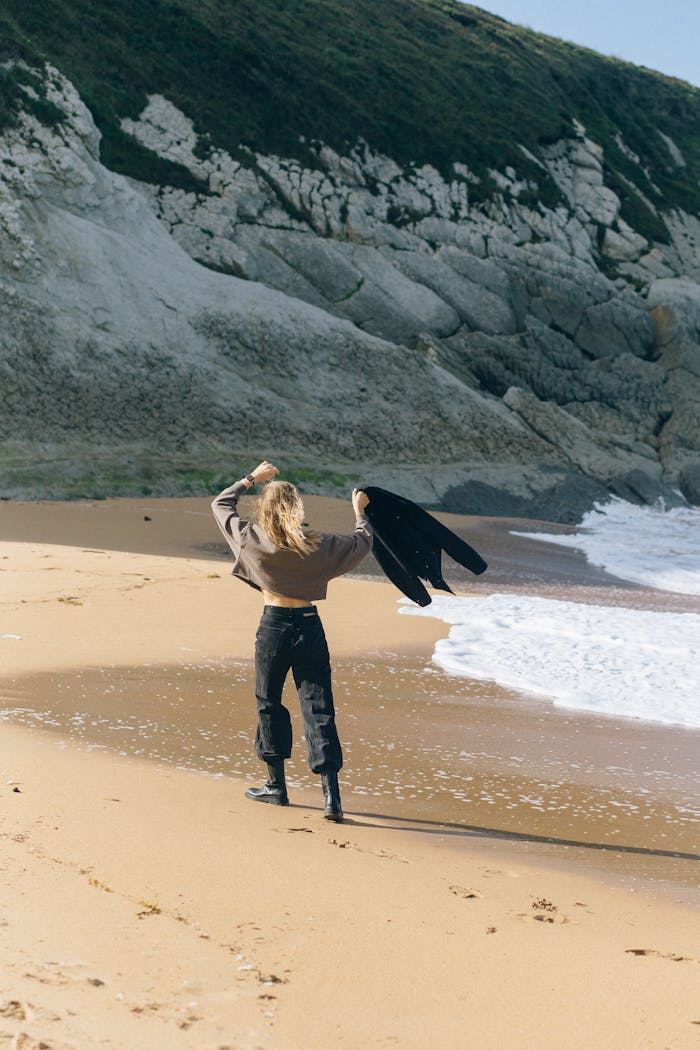 woman in brown jacket and black pants standing on beach shore 5712965